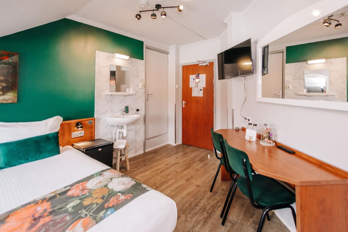 Ein Hotelzimmer mit Bett, Schreibtisch mit Stuhl, Waschbecken und einem an der Wand befestigten Fernseher.