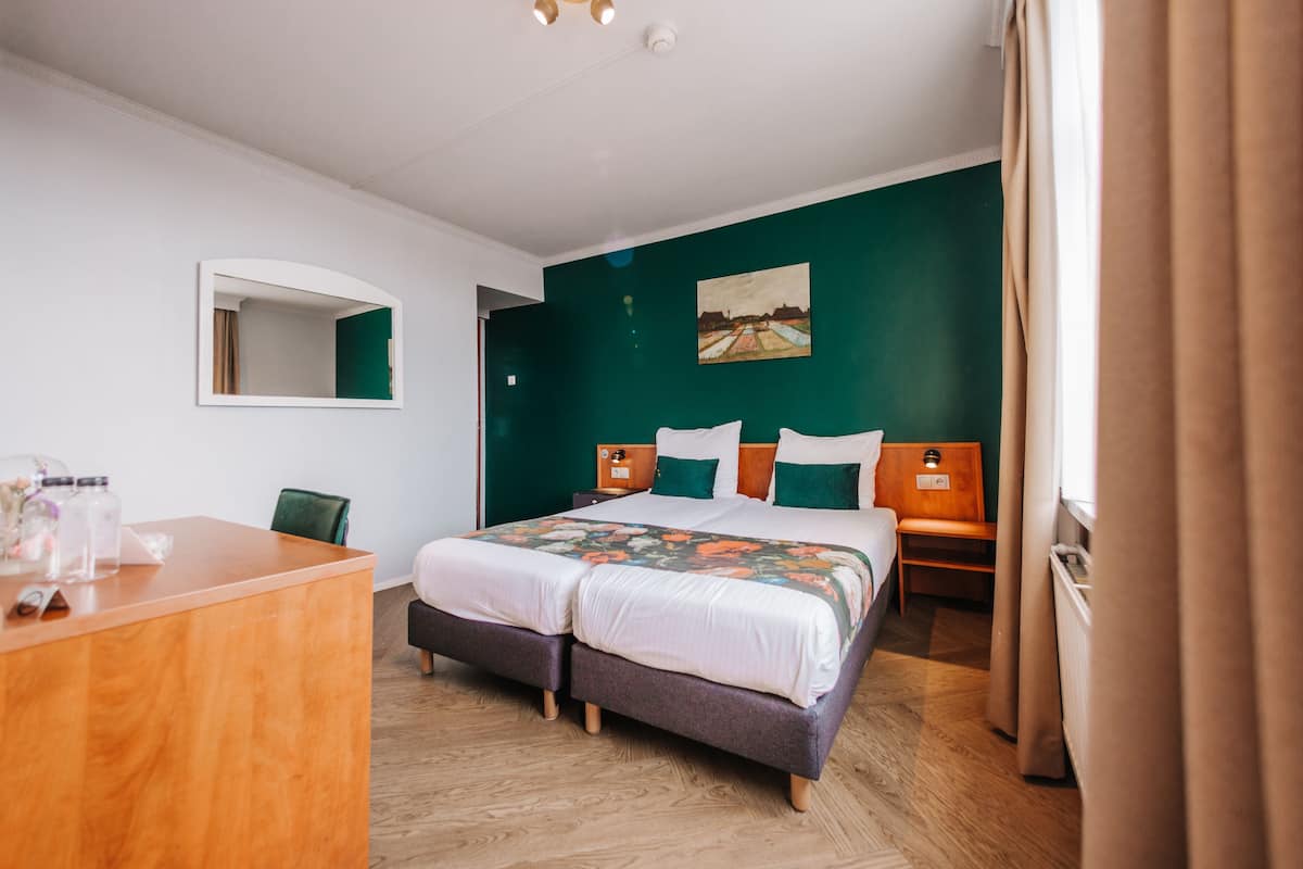 Ein Hotelzimmer mit einem großen Bett, einem Holztisch, einem Spiegel und einer grünen Wand.