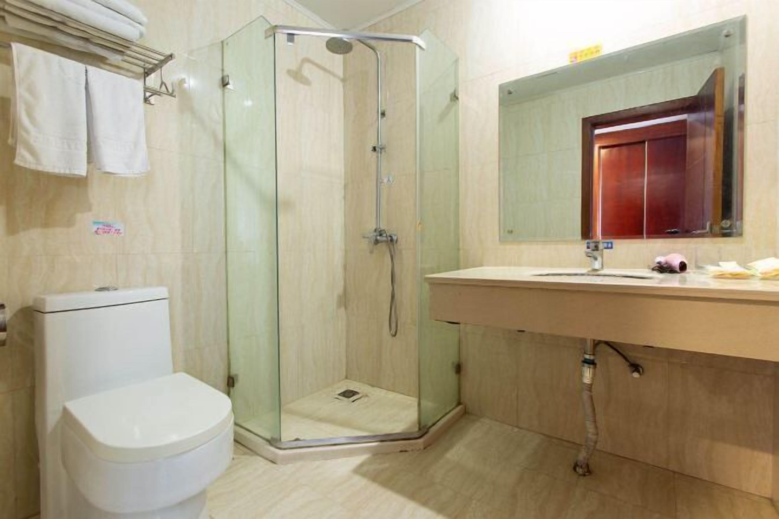 Uma casa de banho com cabine de duche em vidro, sanita branca, lavatório com espelho e um porta-toalhas.