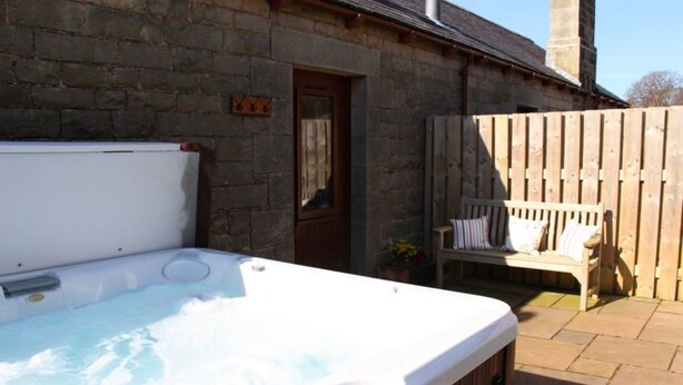 A hot tub in a stone-walled outdoor area with a wooden fence and a bench. - Tower Barn (Brampton)