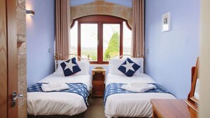 A room with two beds, each with a star-patterned pillow, a wooden headboard, and a window with curtains. - Tower Barn (Brampton)