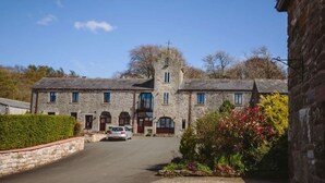 A stone building with a central tower, a driveway, and a car parked in front. - Tower Barn (Brampton)