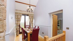 A dining area with a wooden table and red chairs, a chandelier, and a view through a window with curtains. - Tower Barn (Brampton)