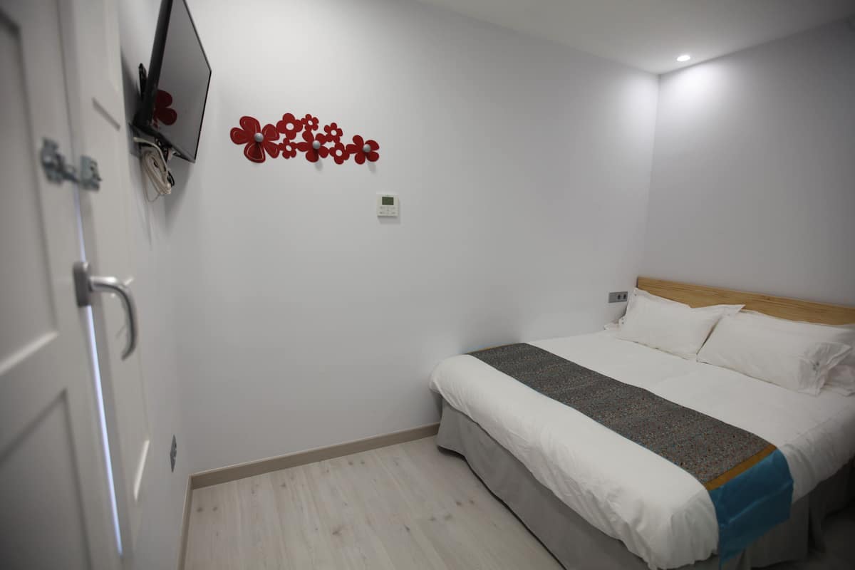 A bedroom with a bed, a TV mounted on the wall, and a thermostat.