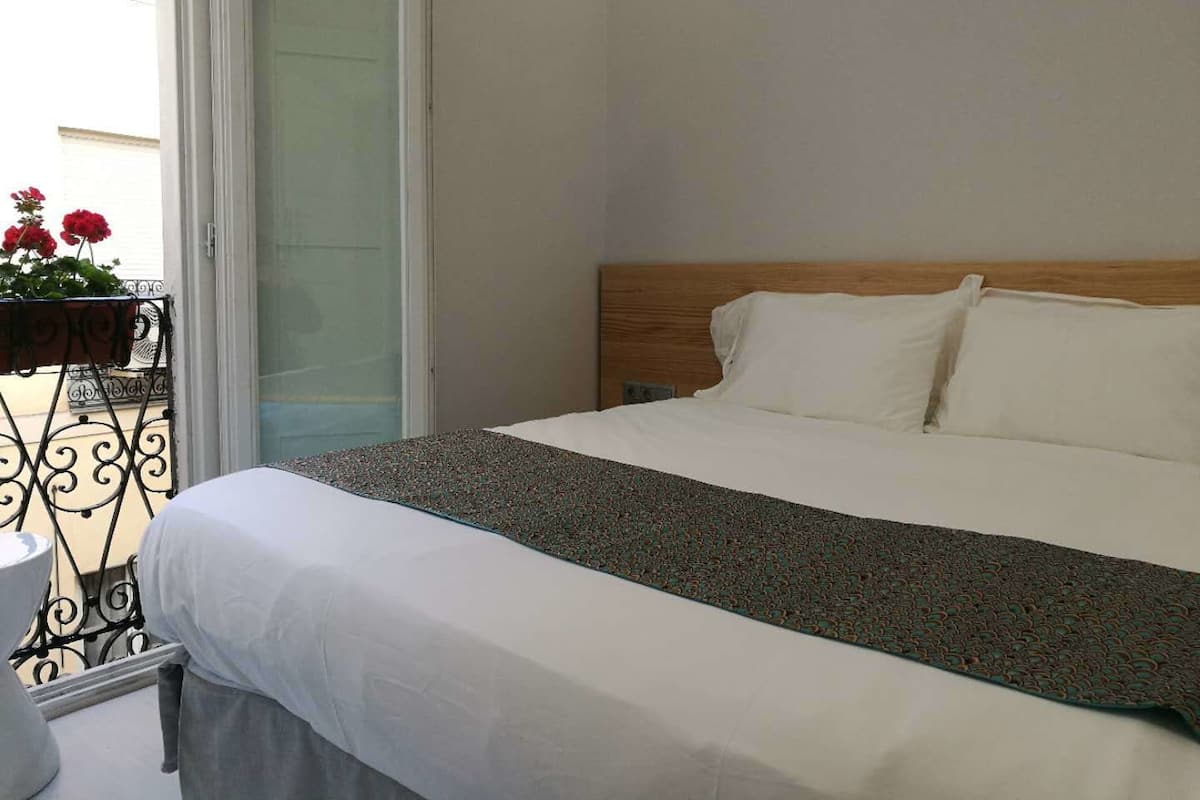 A hotel room with a bed, a wooden headboard, and a balcony with red flowers.