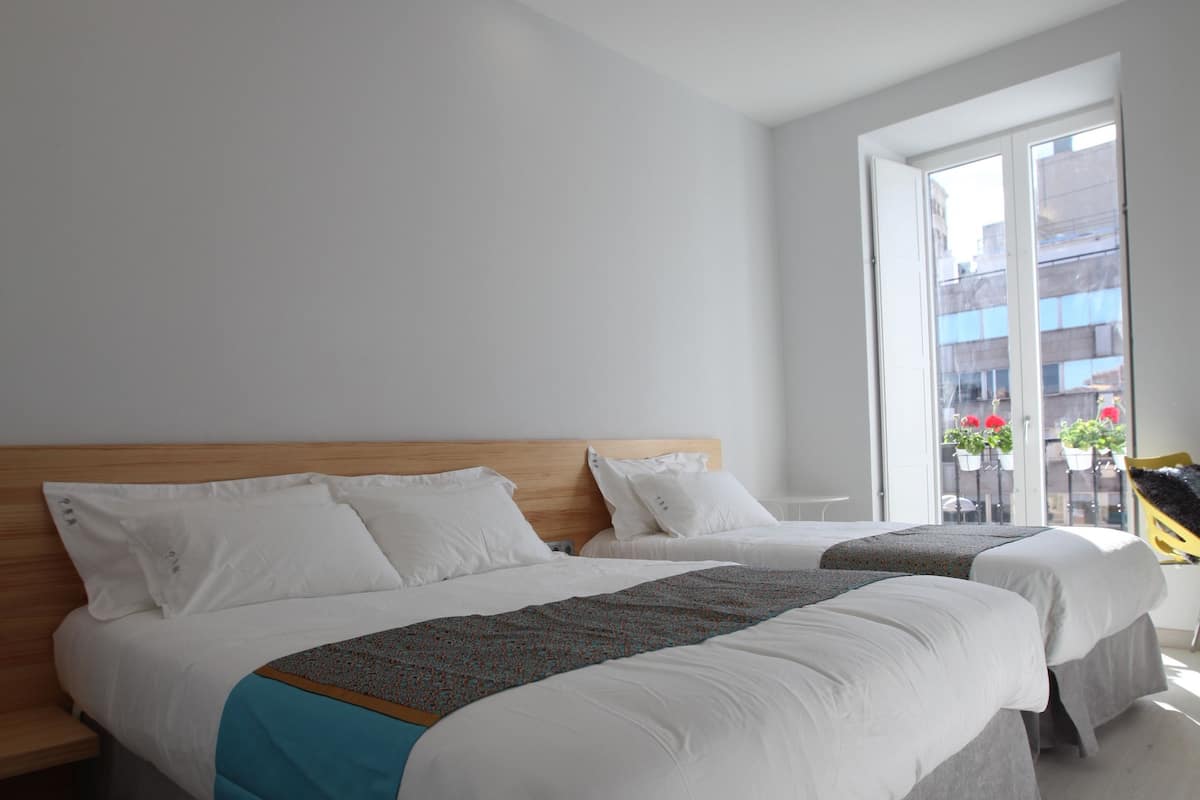 A modern hotel room with two beds, a wooden headboard, and a large window offering a city view.