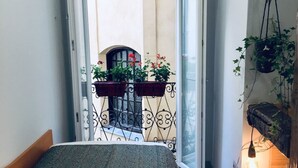 A narrow room with a bed, a balcony with potted plants, and a hanging light fixture. - Hostal Palacio Luna (Madrid)
