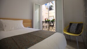 A bedroom with a bed, a chair, and a view of a balcony with plants. - Hostal Palacio Luna (Madrid)