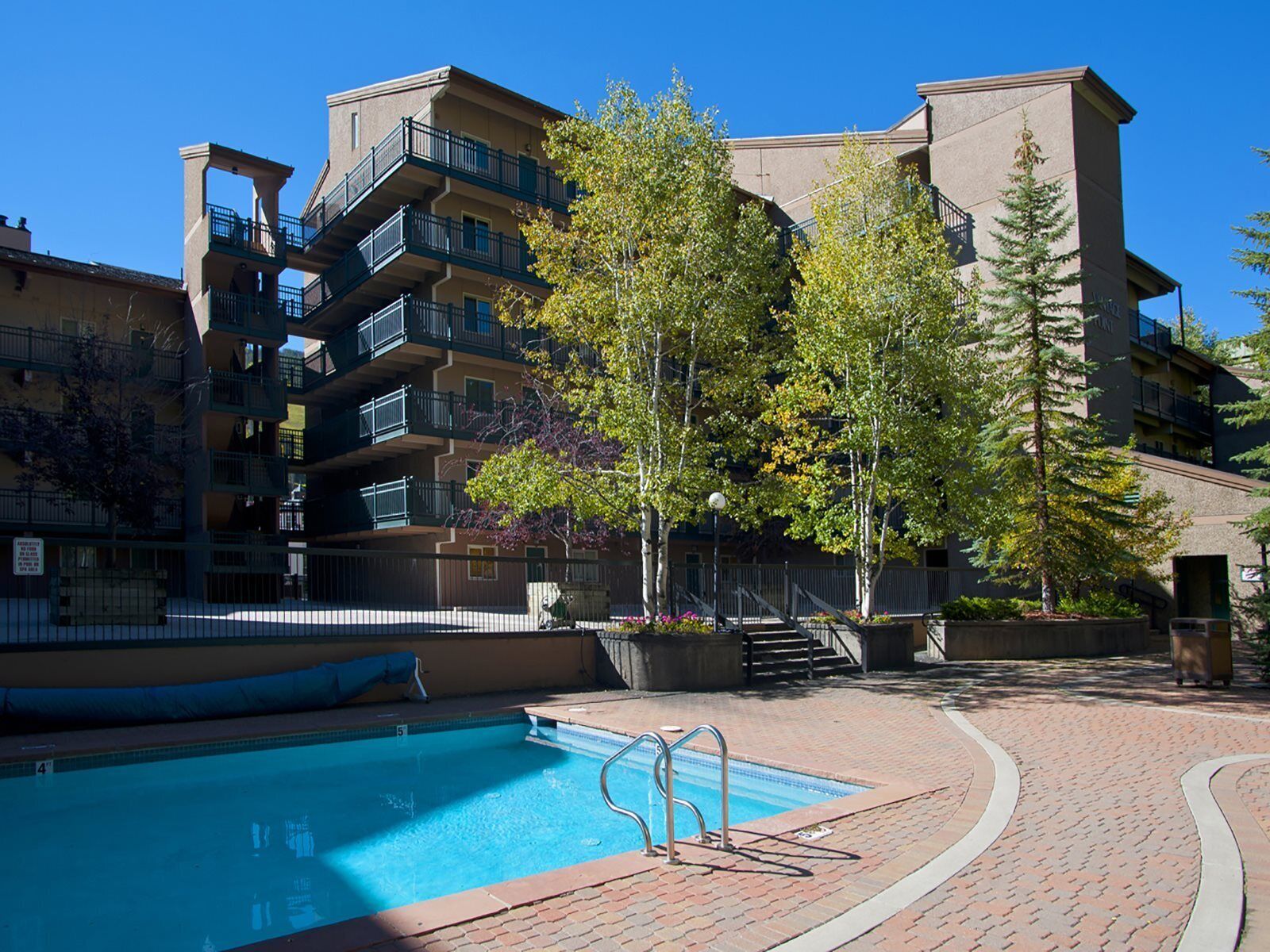 A multi-story building with a swimming pool, outdoor stairs, and a fenced area.