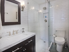 A modern bathroom with a glass shower enclosure, a white toilet, and a marble sink with two faucets.