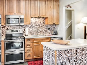 A kitchen with wooden cabinets, a microwave, a stove, a toaster, and a tiled backsplash.