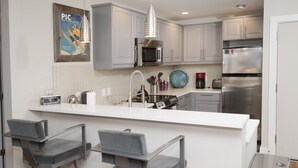 Une cuisine moderne avec des meubles blancs, des appareils en acier inoxydable et un îlot central doté de tabourets de bar.