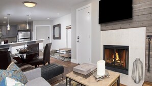 Un salon moderne avec une cheminée, un coin repas et une cuisine en arrière-plan.