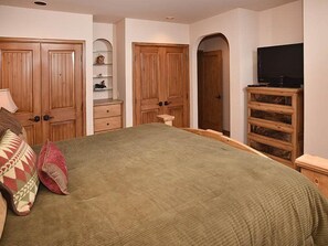 A bedroom with a bed, wooden wardrobe, a television, and a dresser.