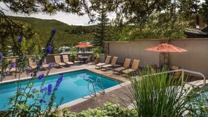 A pool area with lounge chairs and umbrellas, surrounded by greenery and a view of hills. - Pines Townhome (Avon)
