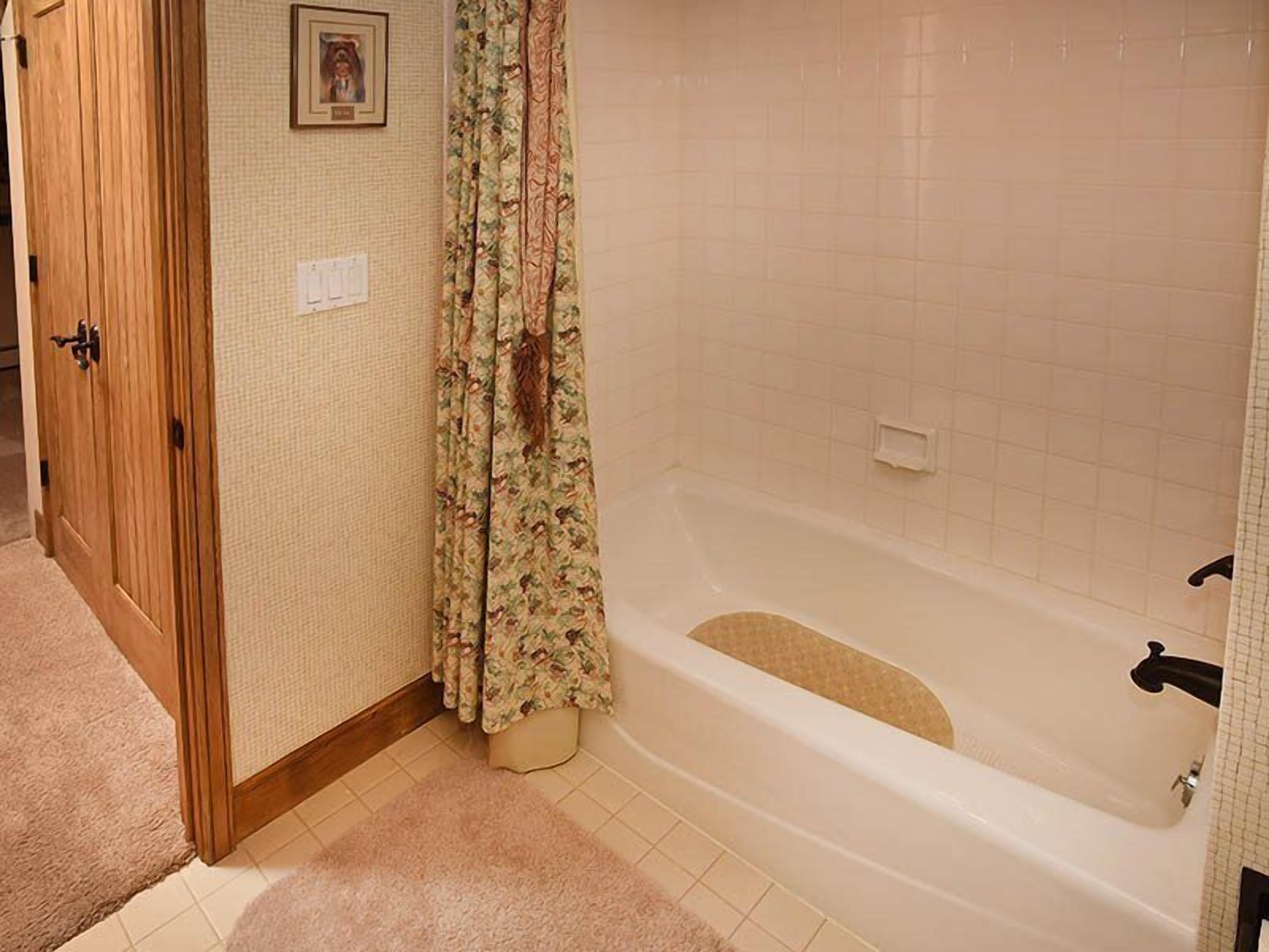 A bathroom with a bathtub, wooden door, and floral curtains.