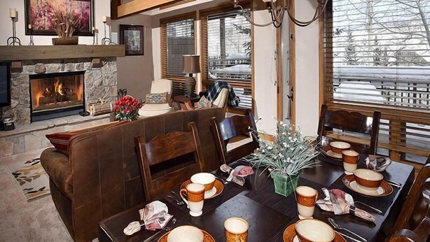A cozy dining area with a fireplace, wooden beams, and a large window with a view. - Pines Townhome (Avon)