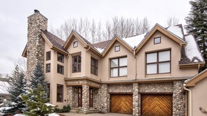 A multi-story house with a stone facade, large windows, and a garage with wooden doors. - Vermont Road Chalet (Vail)