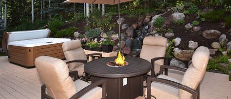 A deck with a round table, four chairs, a fire pit, a sofa, and an umbrella.