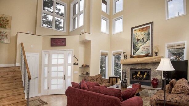 A spacious living room with a fireplace, a large window, and a high ceiling. - Vermont Road Chalet (Vail)