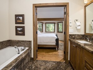 Une salle de bain d’hôtel dotée d’une grande baignoire, d’un chambranle en bois menant à une chambre, et d’un comptoir en marbre.