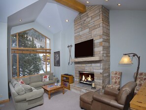 A cozy living room with a stone fireplace, a large window overlooking a snowy landscape, and comfortable seating. - Cascades On Gore Creek (Vail)