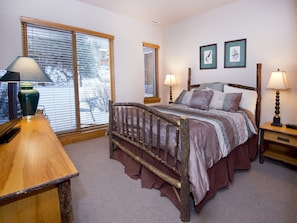 A bedroom with a wooden bed frame, two bedside lamps, a wooden nightstand, and a window with blinds. - Cascades On Gore Creek (Vail)
