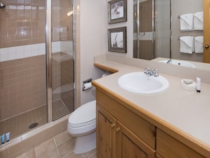 A bathroom with a glass-enclosed shower, a white toilet, a sink with a mirror, and framed pictures on the wall. - Cascades On Gore Creek (Vail)