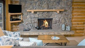 Ein gemütliches Wohnzimmer mit Kamin aus Stein, einem flachbildfernseher an einer Holzablage und einer komfortablen Sitzecke mit Sofa und Couchtisch.