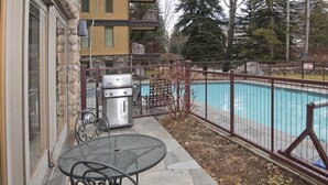 Eine Terrasse mit Grill, Pool und einem Metallzaun.