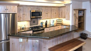 Eine Küche mit Holzausstattung, Edelstahlgeräten, einer Arbeitsplatte aus Granit und einer hölzernen Bank.