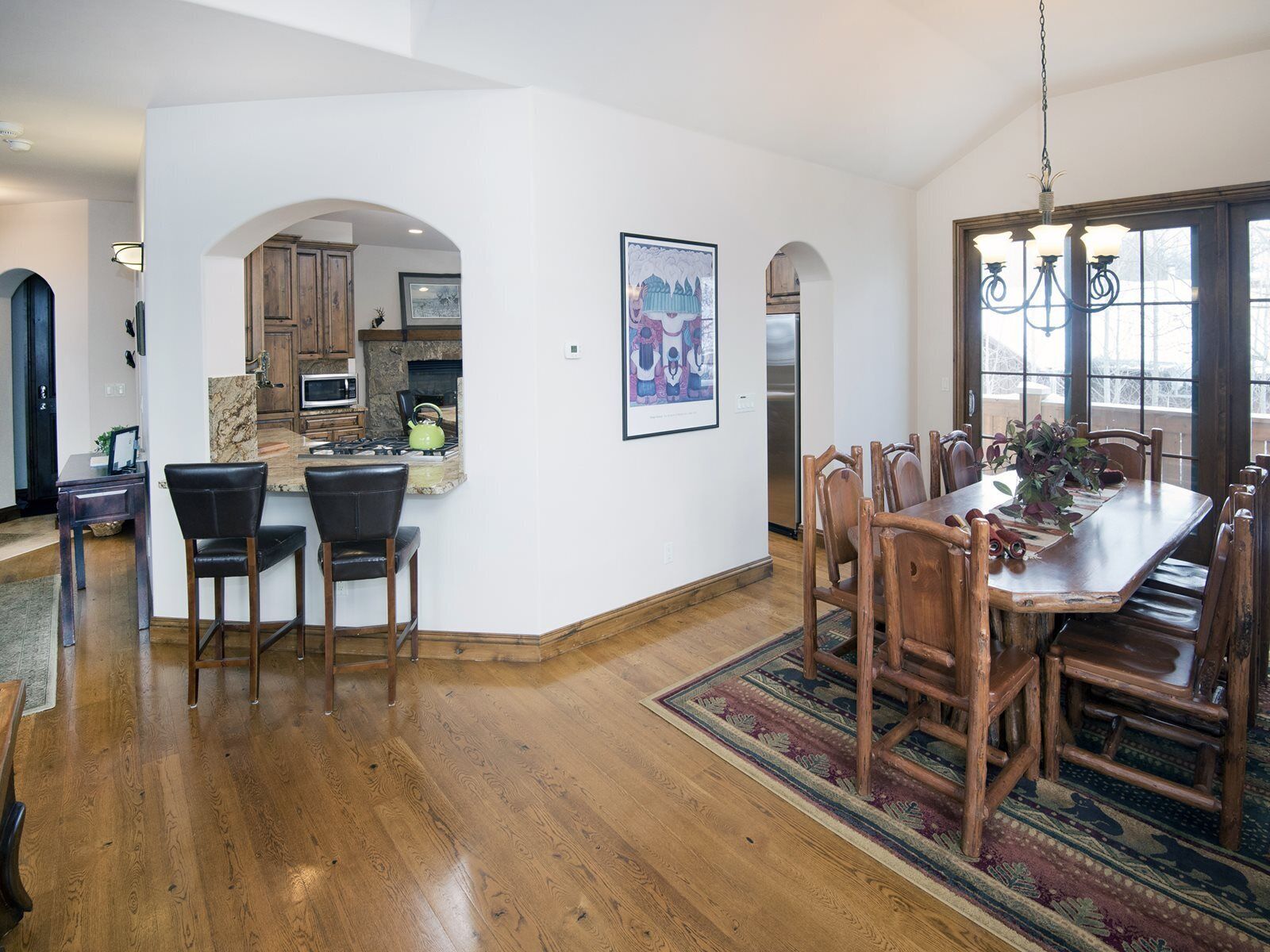 A spacious dining area with a wooden table and chairs, a kitchen with stone countertops, and a large window providing natural light.