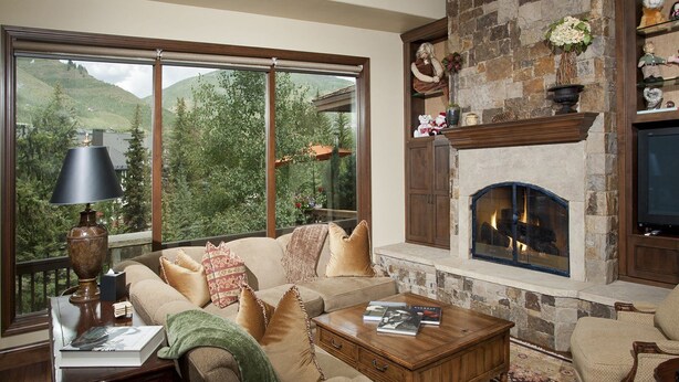 Una sala de estar acogedora con chimenea, un sofá, una mesa de centro y vistas a un paisaje montañoso a través de amplios ventanales.