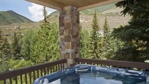 Un jacuzzi en un balcón con un pilar de piedra, rodeado de árboles y un paisaje montañoso.