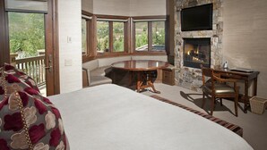 Un dormitorio con una cama grande, una chimenea de piedra, una mesa de comedor y vistas al exterior.