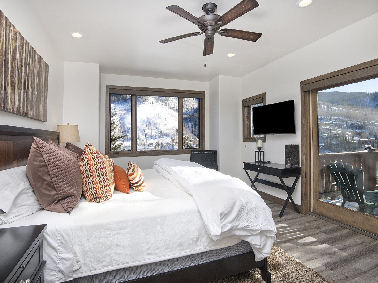 A bedroom with a bed, a desk, a TV, and a balcony with a view.