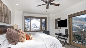 A bedroom with a bed, a desk, a TV, and a balcony with a view. - Glacier Court 1854 A (Vail)