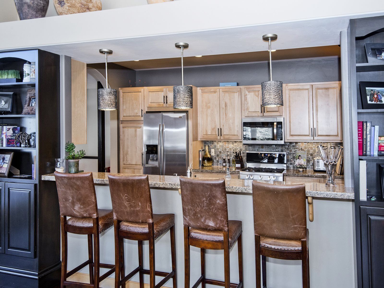 A modern kitchen with a central island, bar stools, stainless steel appliances, and pendant lighting.