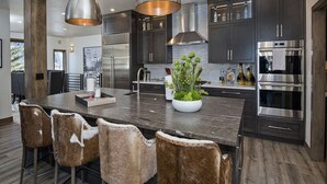 A modern kitchen with dark cabinets, stainless steel appliances, and a central island with bar stools. - Glacier Court 1854 A (Vail)