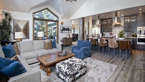 A spacious living area with a large window, a chandelier, and a modern kitchen with bar stools. - Glacier Court 1854 A (Vail)