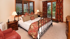 A bedroom with a four-poster bed, wooden nightstands, a red armchair, and a view of the outdoors through large windows. - Glacier Court 1844 B (Vail)