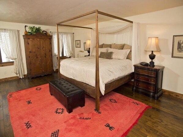 A four-poster canopy bed with a red rug, wooden furniture, and a window with curtains.