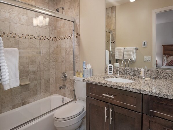 Un baño moderno con ducha de vidrio, bañera, inodoro y tocador con lavamanos y espejo.