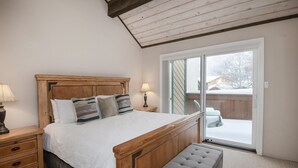A bedroom with a wooden bed, a bench, a nightstand, and a sliding glass door leading to a balcony. - Meadow Ridge Townhome A (Vail)