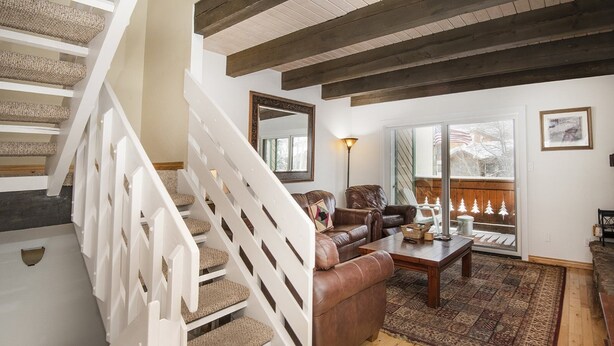 A staircase with beige carpeted steps leading to a living room with a brown leather sofa, a wooden coffee table, and a patterned rug. - Meadow Ridge Townhome A (Vail)