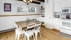 A modern kitchen with white cabinets, a wooden dining table, and white chairs. - Meadow Ridge Townhome A (Vail)