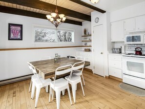 A modern kitchen with white cabinets, a wooden dining table, and white chairs.