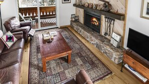 A cozy living room with a fireplace, leather sofas, a coffee table, and a large TV. - Meadow Ridge Townhome A (Vail)