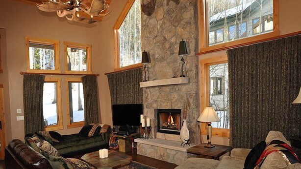 A cozy living room with a stone fireplace, leather sofas, and a large window overlooking a forest. - Meadow Brook Chalet (Vail)