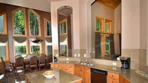 A spacious kitchen with a central island, wooden cabinets, and large windows offering views of the outdoors. - Meadow Brook Chalet (Vail)